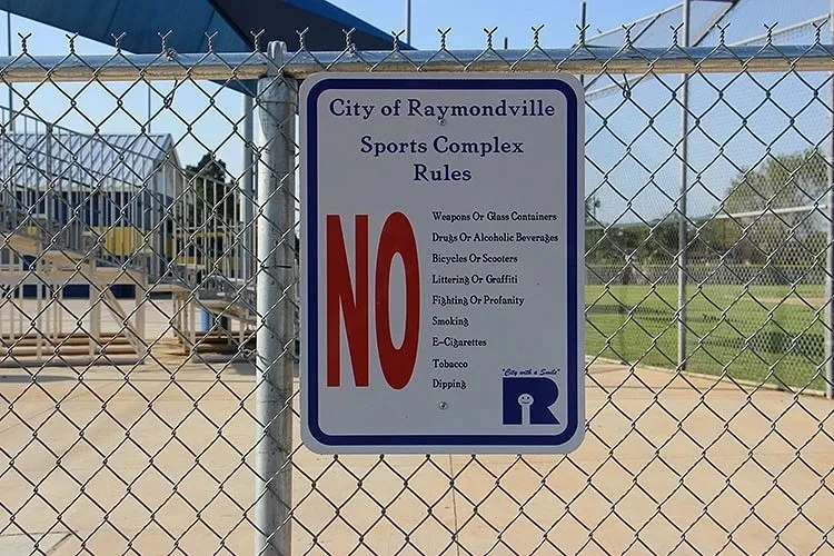 A sign is posted on the fence of a baseball field.